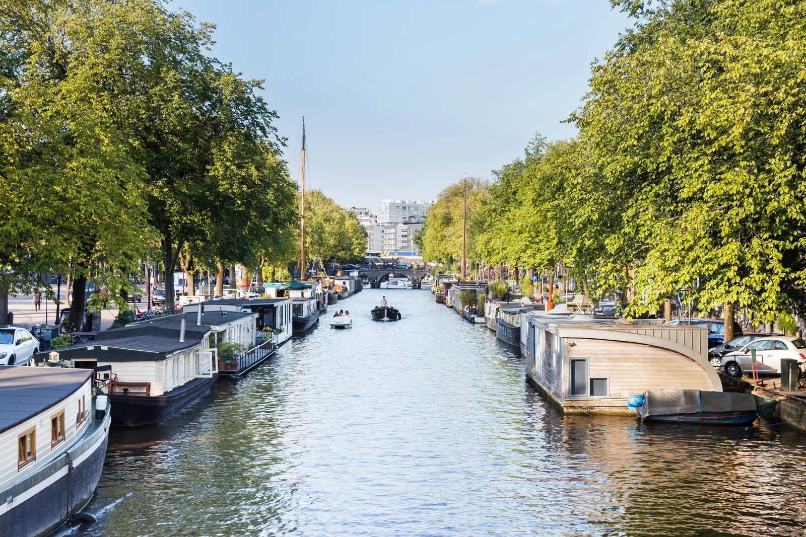 Tree-lined Prinsengracht with moored houseboats, small boats on the water and Lekkeresluis bridge ahead