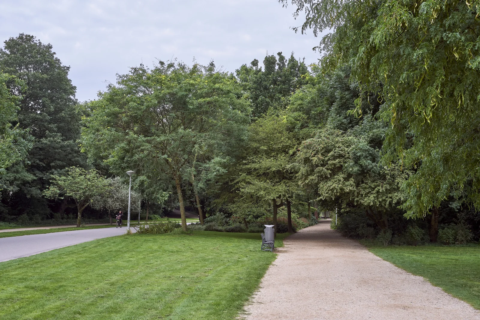 A gravel path and an adjacent paved route through mature trees and lawns in Vondelpark, with a distant cyclist