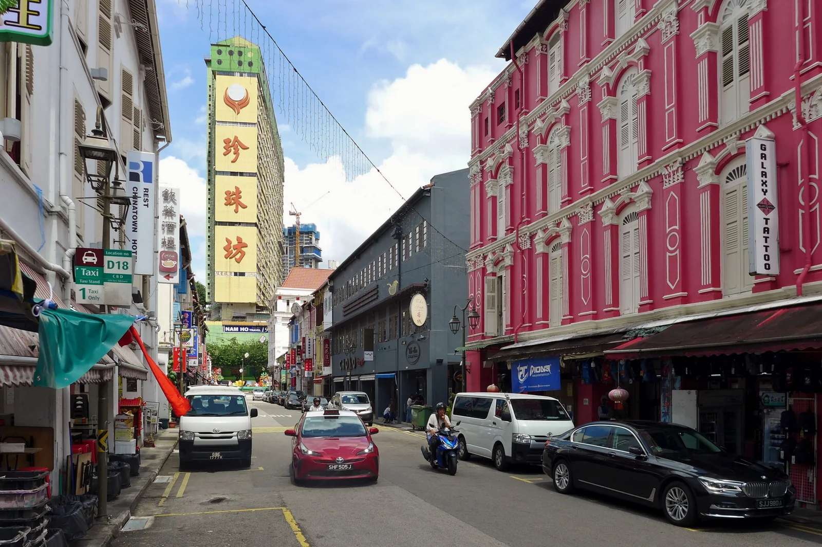 Colourful shophouses lining Temple Street, with vehicles and the tall People’s Park Complex behind them